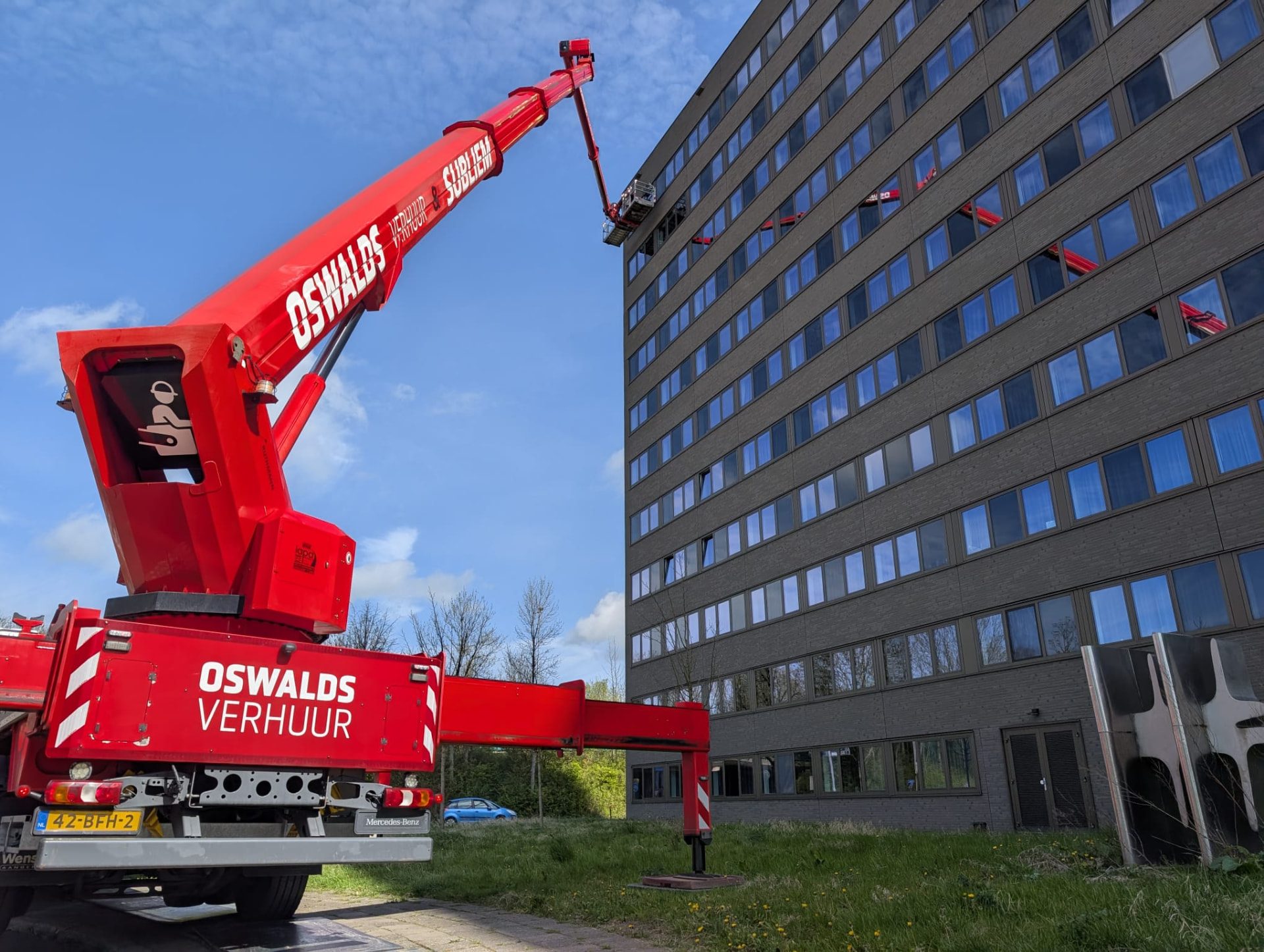Rode Oswalds Verhuur en Subliem vrachtwagenhoogwerker aan het werk bij een hoog kantoorgebouw